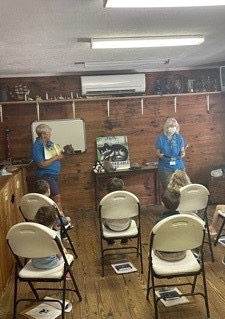 Volunteers Cindy Horn (left) and Debbie Sobien (Right) entertain a homeschool co-op by reading a copy of Nelly: The Lighthouse Cat in the newly reimagined Education Building.